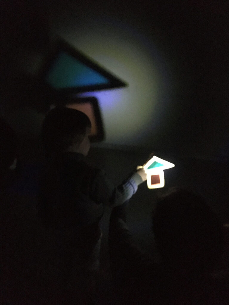 Niño jugando con un triángulo y un cuadrado translucidos formando una casa en los talleres de luz